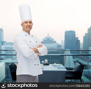cooking, profession and people concept - happy male chef cook with crossed hands over city restaurant lounge background