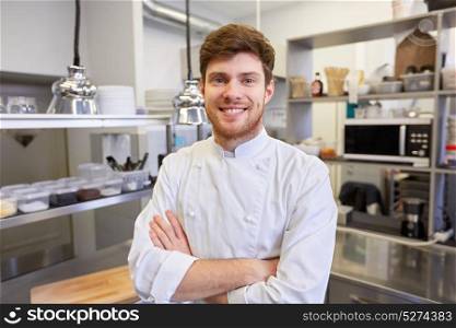 cooking, profession and people concept - happy male chef cook with crossed hands at restaurant kitchen. happy male chef cook at restaurant kitchen
