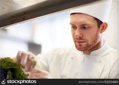 cooking, profession and people concept - happy male chef cook with greens making food at restaurant kitchen. happy male chef cooking at restaurant kitchen