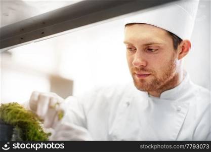 cooking, profession and people concept - happy male chef cook with greens making food at restaurant kitchen. happy male chef cooking at restaurant kitchen