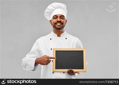 cooking, profession and people concept - happy male indian chef in toque with blank chalkboard for menu over grey background. happy male indian chef in toque with chalkboard
