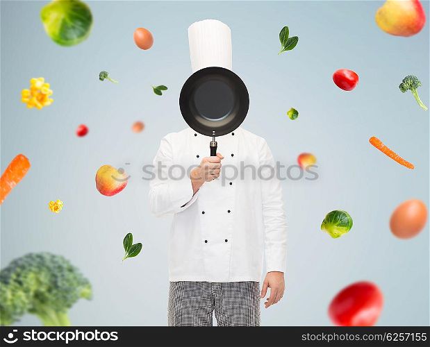 cooking, profession and people concept - male chef cook covering face or hiding behind frying pan over gray background with falling vegetables