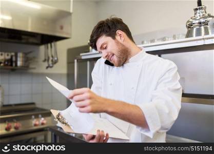 cooking, profession and people concept - male chef cook with clipboard calling on smartphone at restaurant kitchen. chef cook calling on smartphone at restaurant kitchen