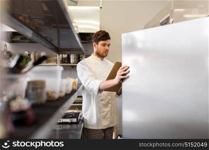cooking, profession and people concept - male chef cook with clipboard doing inventory in restaurant kitchen fridge. chef with clipboard doing inventory at kitchen
