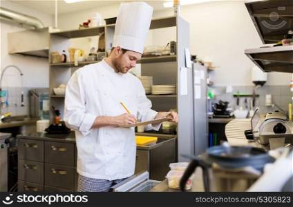 cooking, profession and people concept - male chef cook with clipboard doing inventory of restaurant kitchen fridge. chef with clipboard doing inventory at kitchen