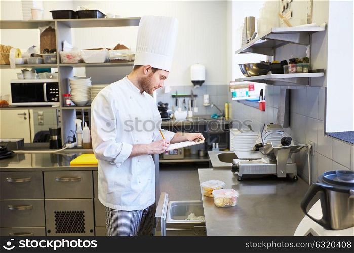 cooking, profession and people concept - male chef cook with clipboard doing inventory and looking to fridge at restaurant kitchen. chef with clipboard doing inventory at kitchen