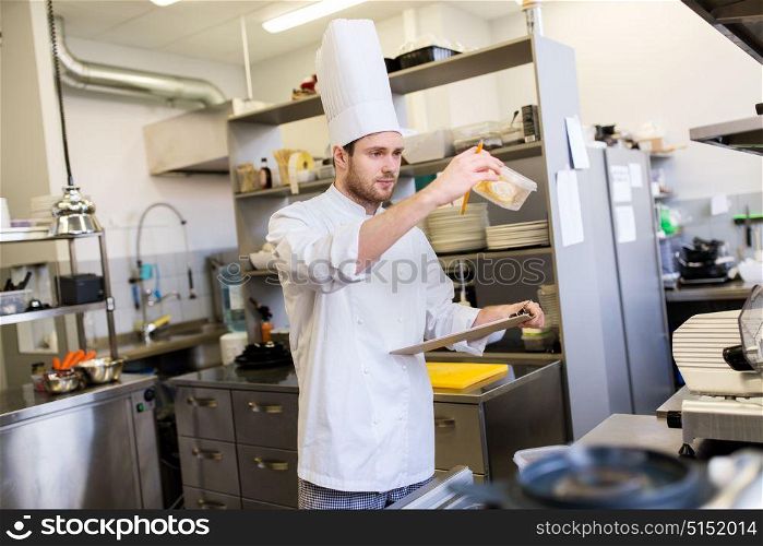 cooking, profession and people concept - male chef cook with clipboard doing inventory in restaurant kitchen. chef with clipboard doing inventory at kitchen