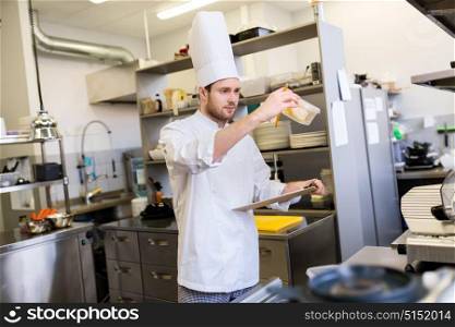 cooking, profession and people concept - male chef cook with clipboard doing inventory in restaurant kitchen. chef with clipboard doing inventory at kitchen