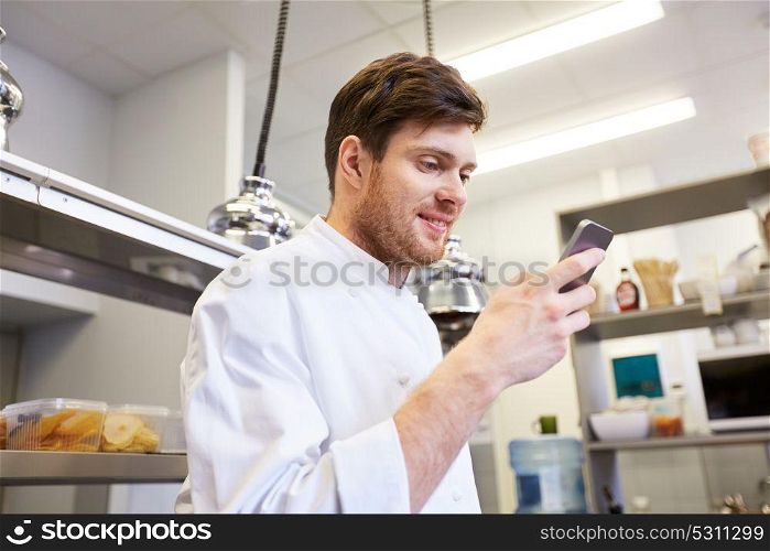 cooking, profession and people concept - male chef cook with smartphone at restaurant kitchen. chef cook with smartphone at restaurant kitchen