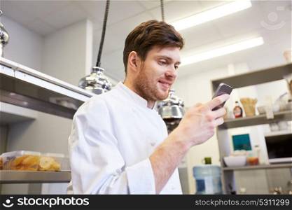 cooking, profession and people concept - male chef cook with smartphone at restaurant kitchen. chef cook with smartphone at restaurant kitchen