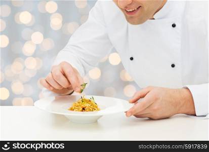 cooking, profession, haute cuisine, food and people concept - close up of happy male chef cook decorating dish over holidays lights background