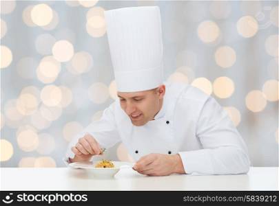 cooking, profession, haute cuisine, food and people concept - happy male chef cook decorating dish over holidays lights background