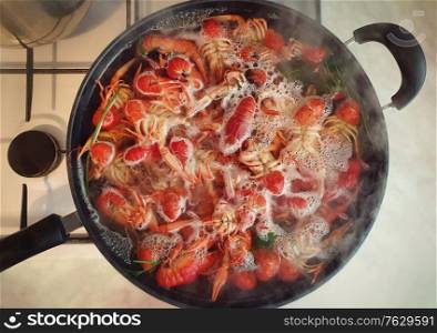 Cooking river crayfish, or crawfish, at home on a traditional recipe. A lot of red, freshwater lobsters boiling in a big bowl on hob. Preparing delicious, non gmo, organic food in house conditions.