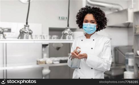 cooking, safety and health concept - female chef in protective medical mask and toque applying hand sanitizer or liquid soap over restaurant kitchen background. female chef in mask with hand sanitizer on kitchen