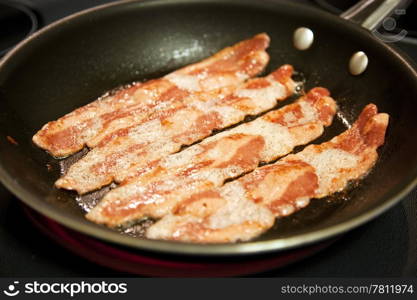 Cooking slices of healthy, low fat turkey bacon in a frying pan. Shallow depth of field.