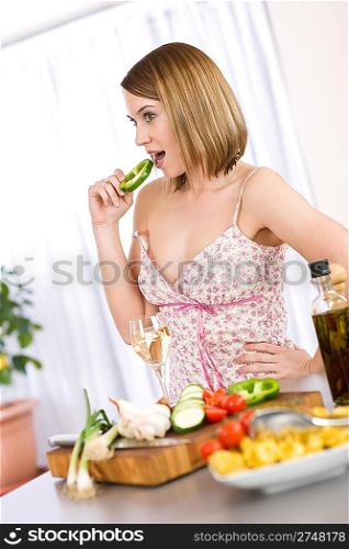 Cooking - smiling woman with glass of white wine and vegetable in modern kitchen