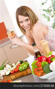 Cooking - smiling woman with glass of white wine and vegetable in modern kitchen
