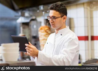 cooking, technology and people concept - happy male chef cook with tablet pc computer at kebab shop. chef cook with tablet pc at restaurant kitchen