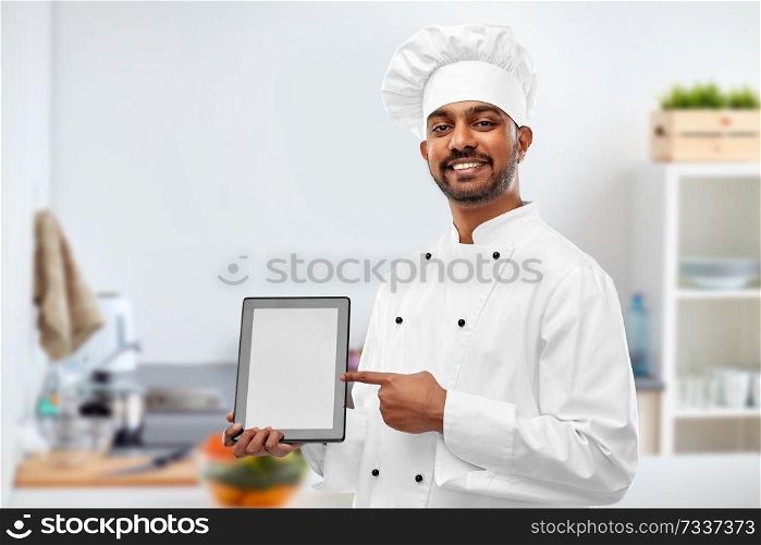 cooking, technology and people concept - happy male indian chef in toque with tablet computer over kitchen background. happy indian chef with tablet computer at kitchen