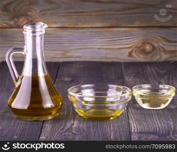 Cooking vegetable oil in a small glass cup and jug on old wooden table