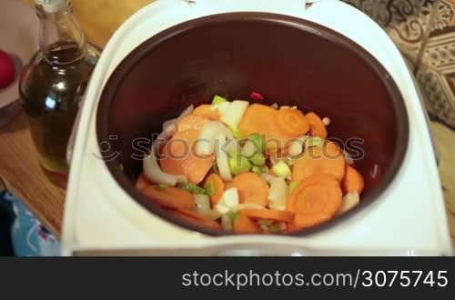 Cooking woman adding chopped tomatoes with knife from wooden cutting board into multicooker and stirring slowly ingredients with spatula