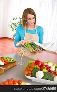 Cooking - Woman reading cookbook for recipe in modern kitchen with vegetable and pasta