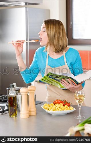 Cooking - Young woman tasting Italian tomato sauce in modern kitchen, with tomatoes and tortellini pasta