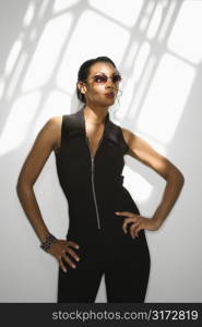 Cool African American mid-adult woman dressed in black standing with hands on hips wearing sunglasses.