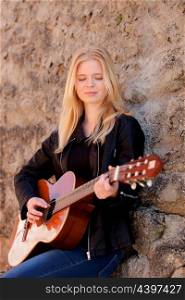 Cool blonde girl playing guitar leaning against a stone wall