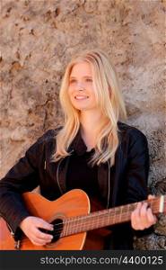 Cool blonde girl playing guitar leaning against a stone wall