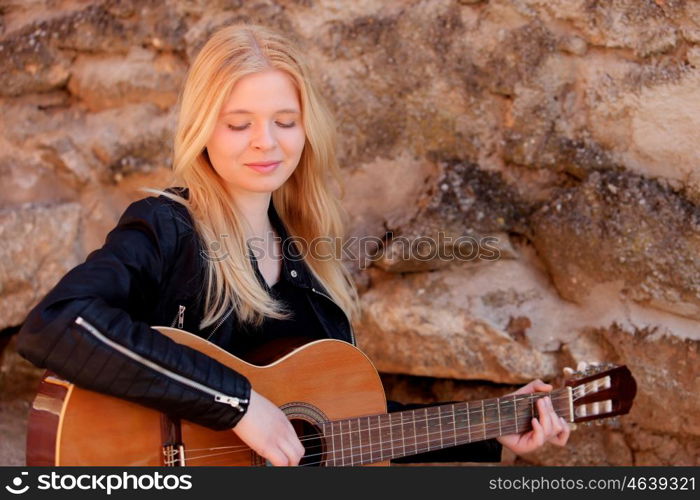 Cool blonde girl playing guitar leaning against a stone wall