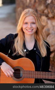 Cool blonde girl playing guitar leaning against a stone wall