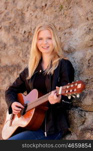 Cool blonde girl playing guitar leaning against a stone wall