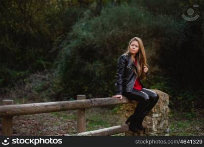 Cool blonde girl sitting on a wooden fence in the park