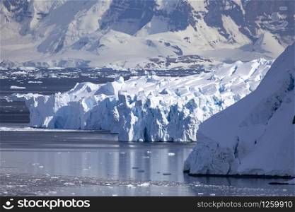 Cool bluish ice from glacier flows into sea in bay with mountains in Antarctica