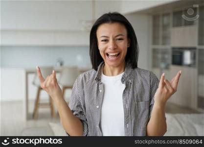 Cool girl shows rock gesture. Conceptual portrait of young attractive emotional woman. Advertising banner mockup. Handsome excited european girl is posing at home. Modern interior of apartment.. Cool girl shows rock gesture. Conceptual portrait of young attractive emotional woman.