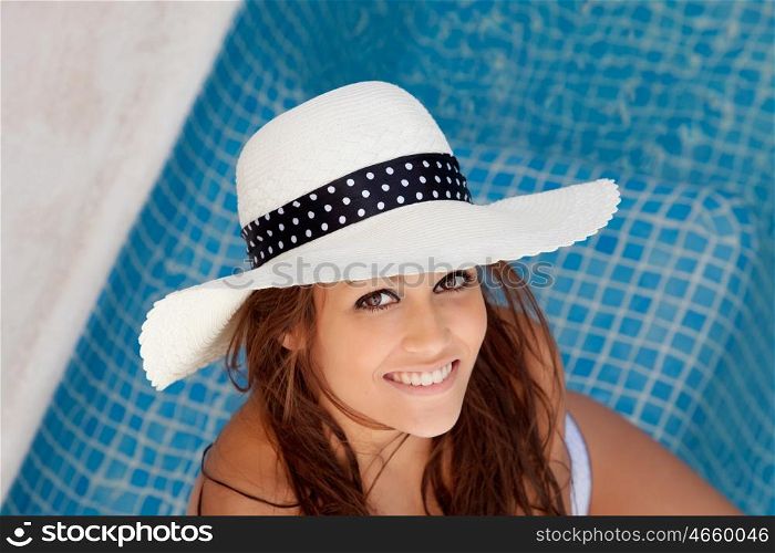 Cool tanned young woman with hat sitting poolside