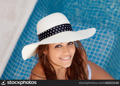 Cool tanned young woman with hat sitting poolside