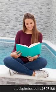 Cool young girl reading a book sitting on the edge of the pool with a waterfall in the background