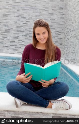 Cool young girl reading a book sitting on the edge of the pool with a waterfall in the background
