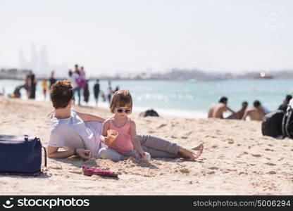 cool young mom and her little girl playing with a bucket full of sand wearing sunglasses and relaxing on the beach on a sunny day