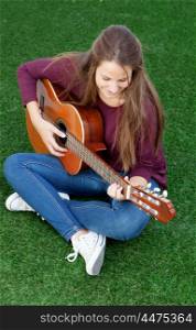 Cool young woman sitting on the grass playing guitar