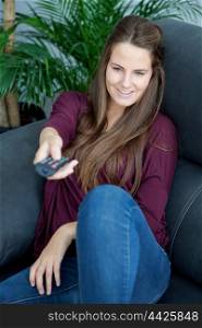 Cool young woman sitting on the sofa at home with a remote control