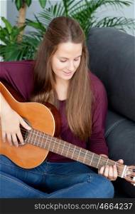 Cool young woman sitting on the sofa playing guitar