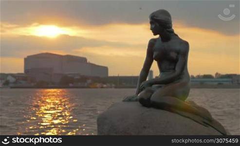 COPENHAGEN, DENMARK - SEPTEMBER 10, 2015: The Little Mermaid bronze statue on water and city background at sunset. One of the major symbols of the city