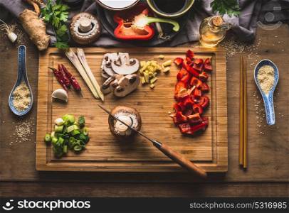 Copped vegetables ingredients for tasty vegetarian stir fry dishes on wooden cutting board with knife and chopsticks, top view. Asian cuisine. Healthy eating and food concept