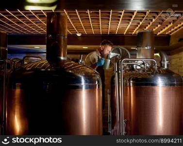 Copper boil kettle and distillery tanks in craft beer brewery. Male brewer owner working at production line checking quality while looking into opened vat. Copper boil kettle and distillery tanks in craft beer brewery