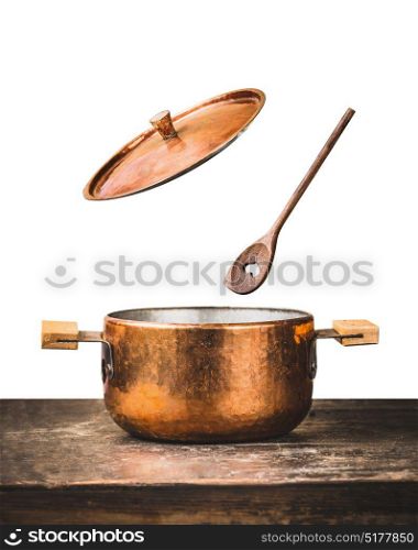 Copper cooking pot with flying open lid and wooden spoon on table, isolated on white background, front view