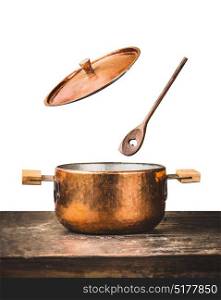 Copper cooking pot with flying open lid and wooden spoon on table, isolated on white background, front view