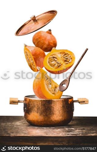 Copper cooking pot with flying pumpkin with knife , open lid and wooden spoon on table, isolated on white background , front view. Autumn seasonal recipes and eating concept